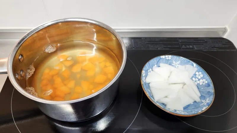 Carrots simmering in clear broth with sliced daikon radish ready to add