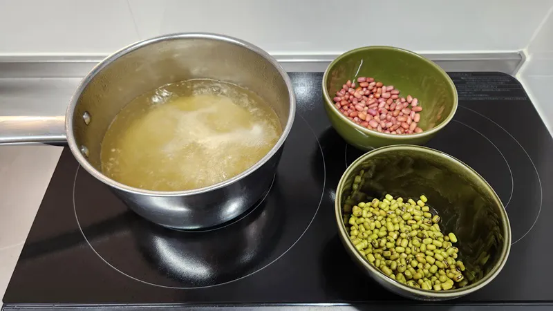 乾燥した赤豆と緑豆のボウルの横で煮立つだし。
