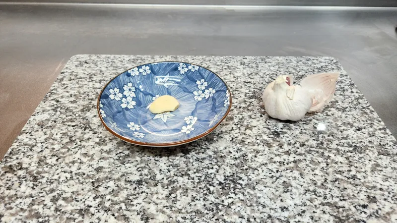 Whole garlic bulb and a peeled clove on a kitchen surface
