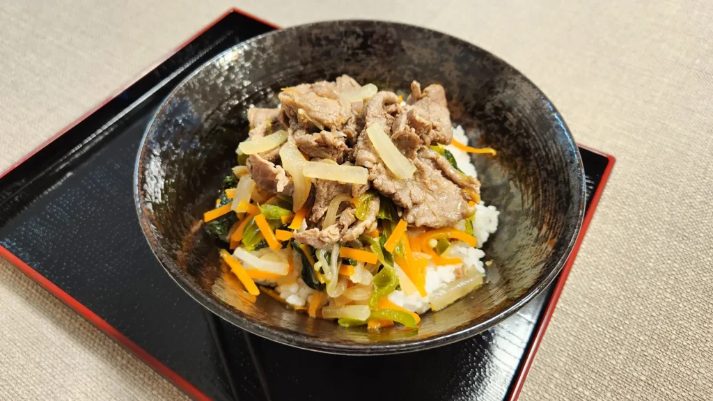 Close-up of sliced beef and vegetables over rice in a Japanese bowl