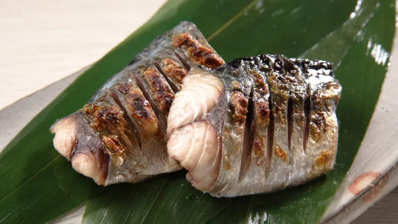 Morceaux de poisson grillé à la peau croustillante servis sur une feuille de bambou verte.
