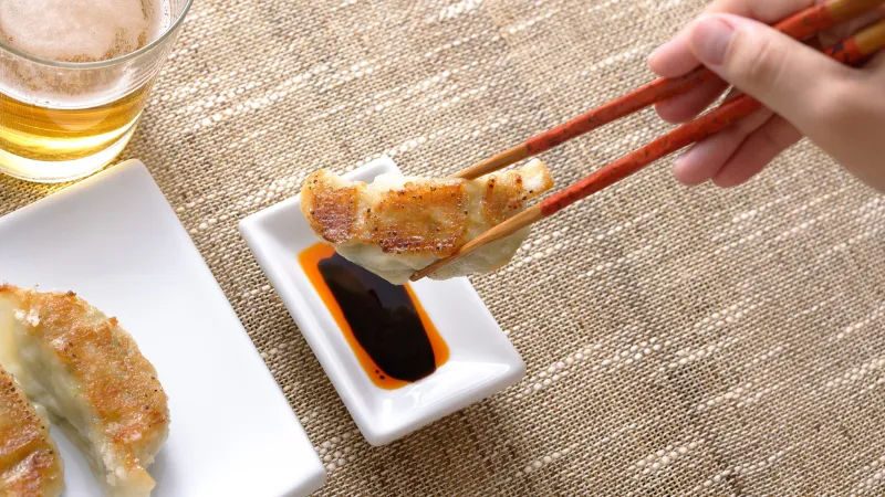 Gyoza dumpling being dipped into soy sauce with chopsticks
