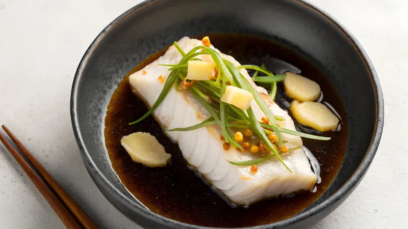 Cooked fish served in a bowl with soy-based sauce and garnishes