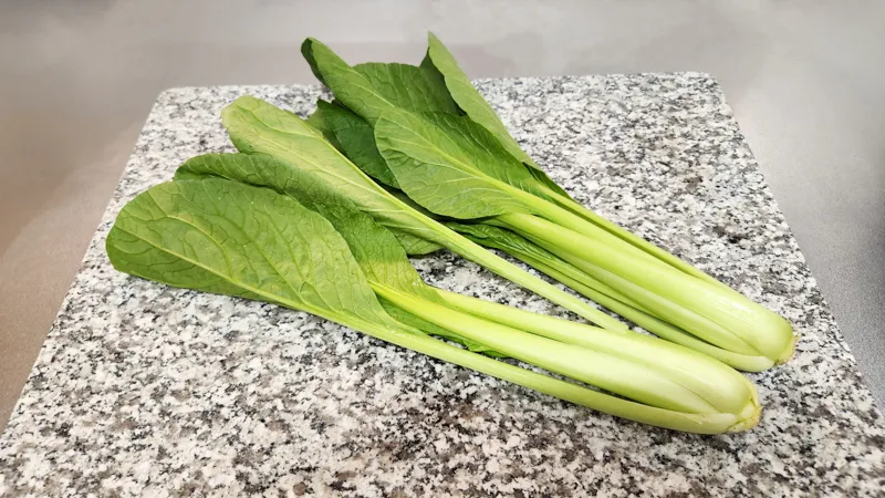 Whole fresh komatsuna greens on a kitchen surface