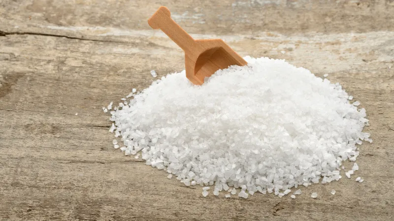 Pile of coarse salt with a small wooden scoop on a wooden surface