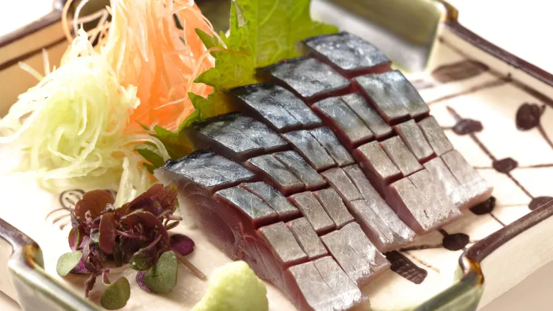 Sashimi de poisson cru servi avec une garniture sur une assiette rectangulaire.
