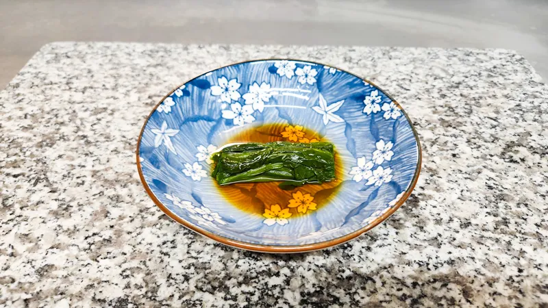 Blanched spinach salad neatly arranged in sauce in a Japanese bowl