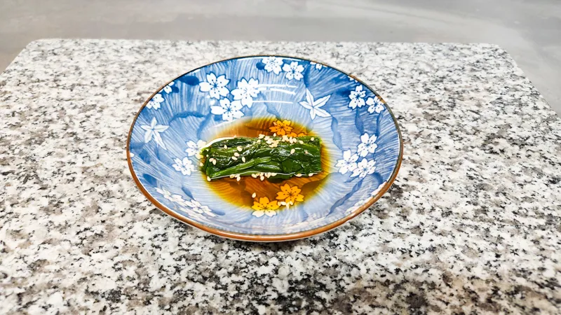 Japanese spinach salad dish topped with sesame seeds in a decorative bowl