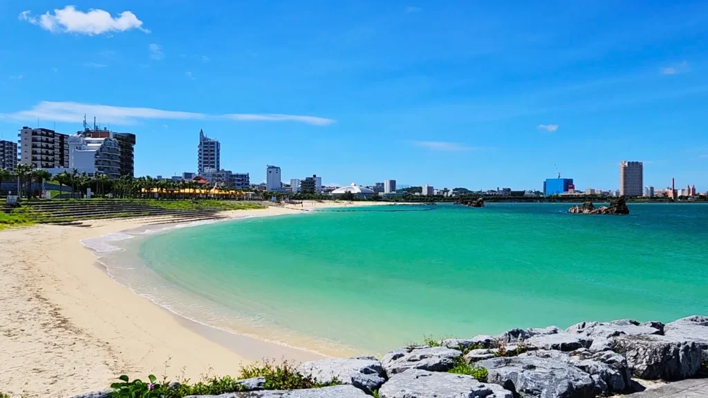 Curved beach with green water and city buildings at Sunset Beach Chatan Okinawa