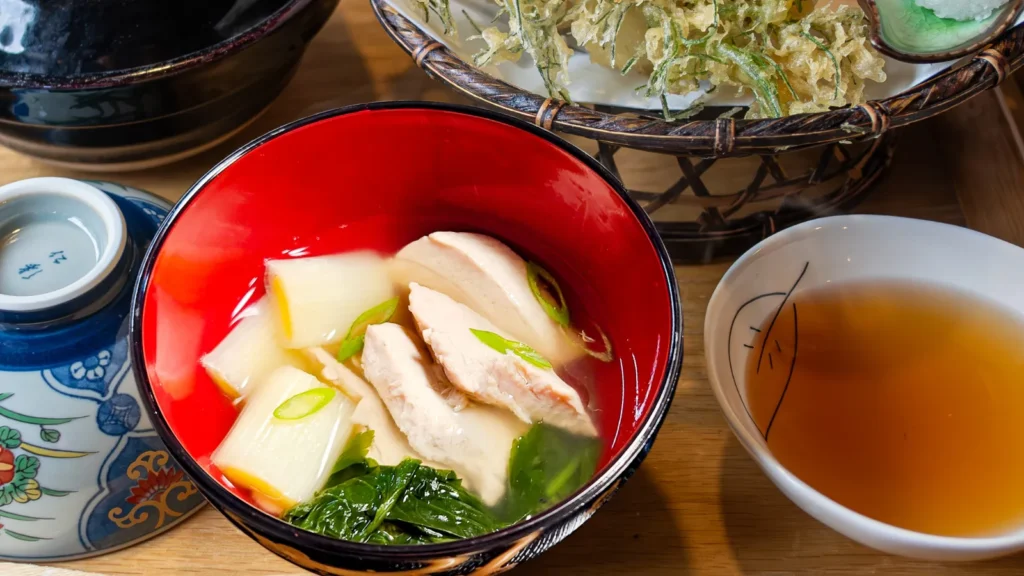 Clear Japanese soup with bluefin tuna slices, leek and leafy greens in a red bowl