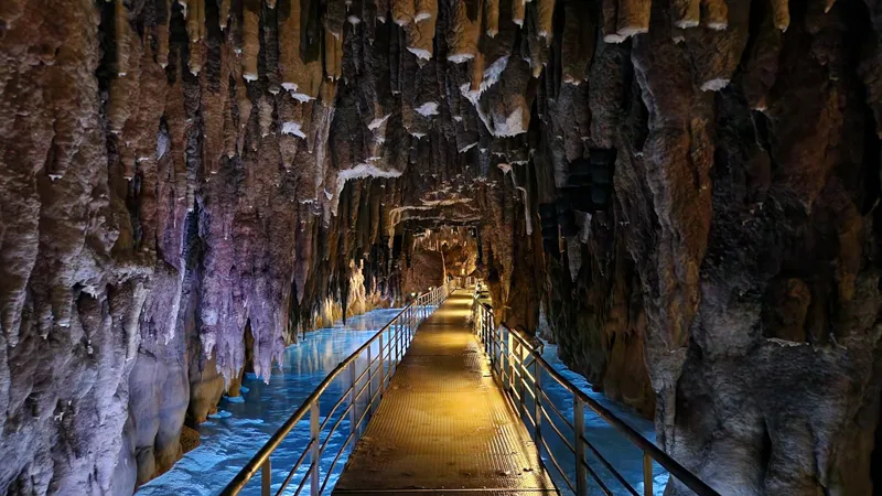 Walkway leading into a limestone cave with stalactites and blue-lit water