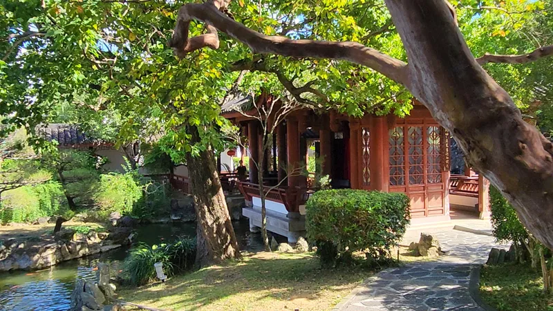 Wooden Chinese style pavilion next to a pond surrounded by trees in Fukushuen chinese Garden Okinawa