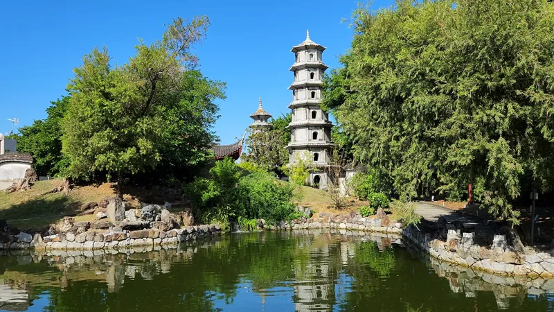 Stone pagoda reflected in a pond surrounded by trees at Fukushuen chinese Garden Okinawa