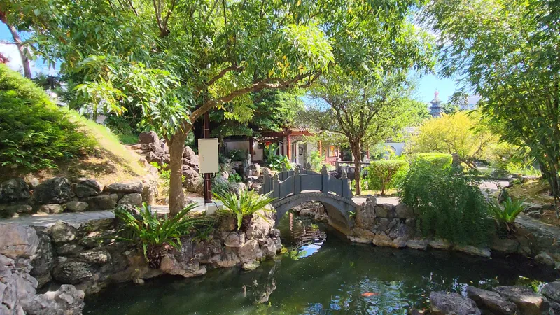 Small stone bridge crossing a pond surrounded by trees in Garden Okinawa