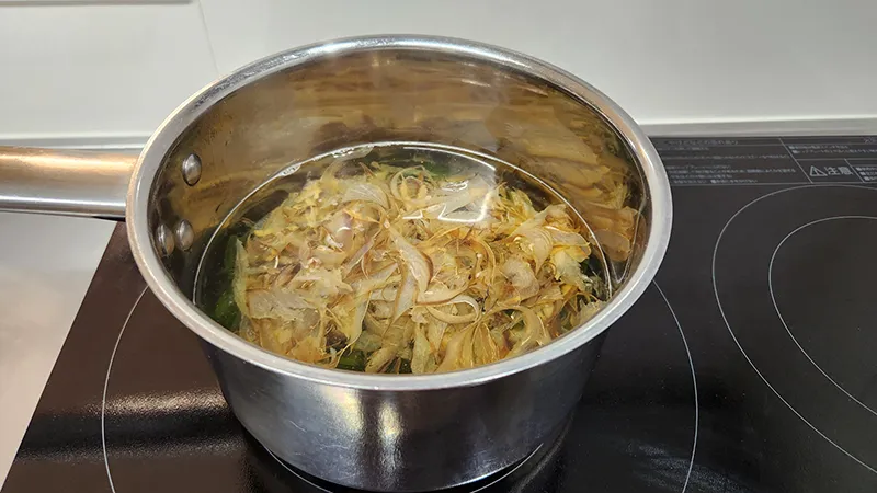 Pot of clear dashi broth infused with dried fish flakes on stovetop