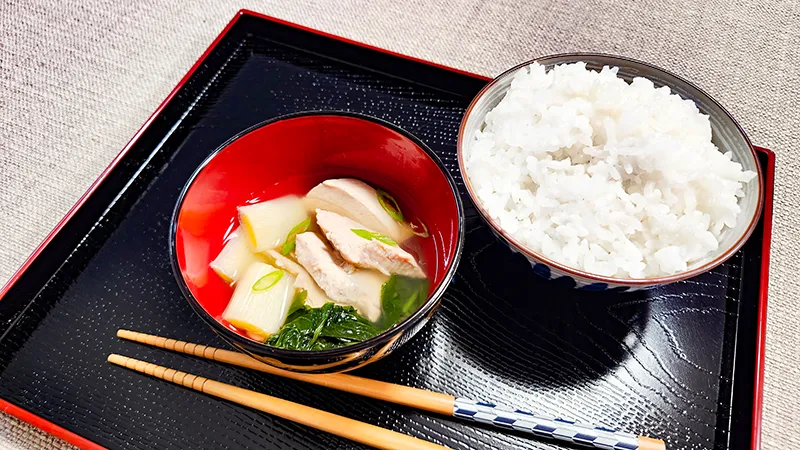Red bowl of tuna soup with rice and chopsticks on serving tray