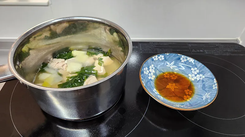 Japanese tuna soup simmering with greens and leek in saucepan