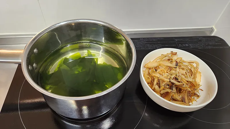 Pot with wakame seaweed in water next to a bowl of dried fish flakes